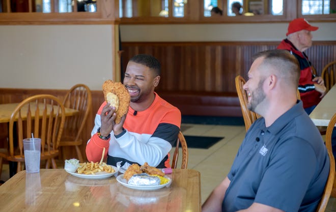 "America's Best Restaurants" host J Russell, left, gets a kick out of the size and heart shape of a tenderloin during filming of an episode of the online show at the Busy Corner restaurant Wednesday, March 13, 2024 in Goodfield.
